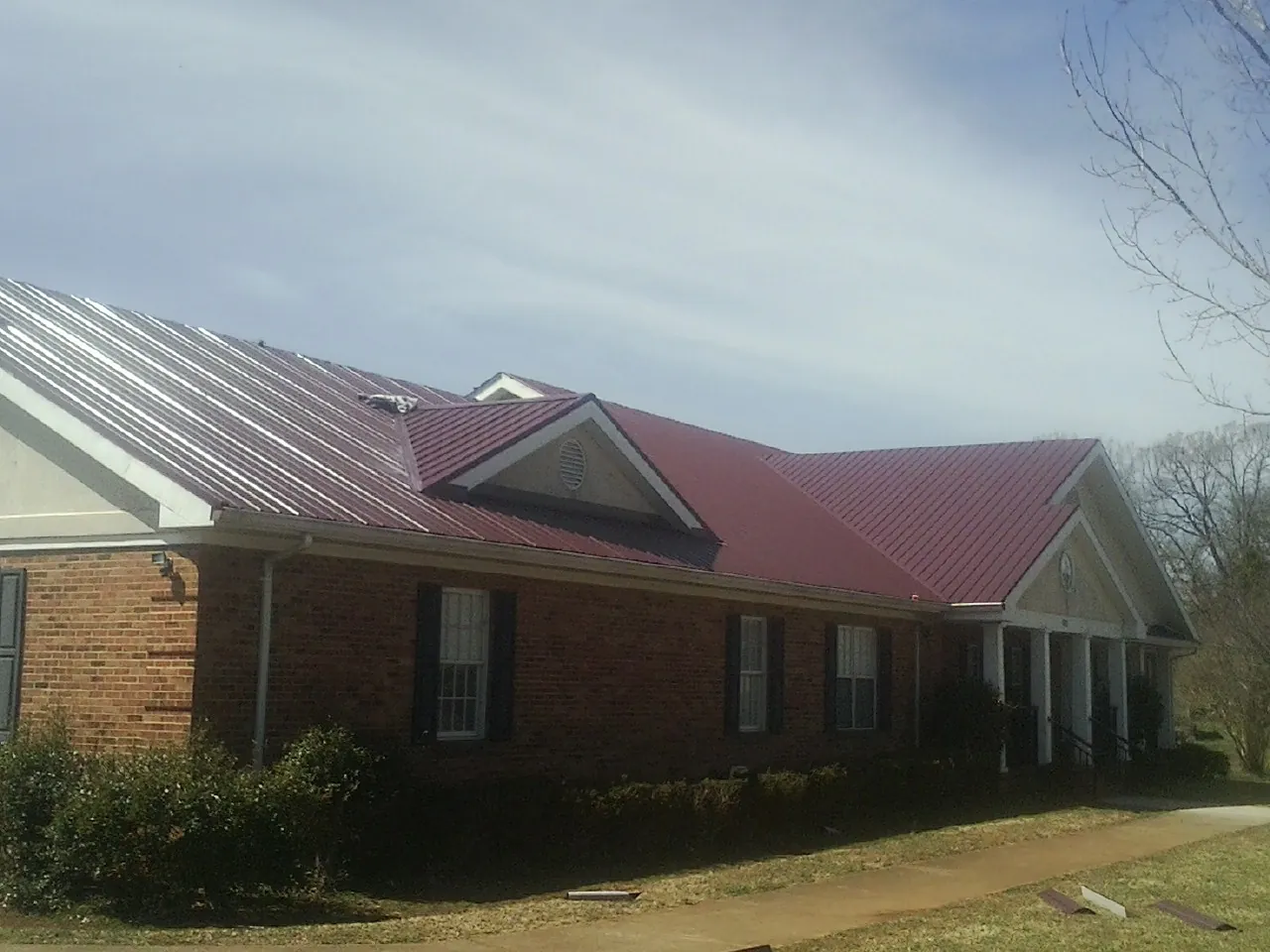 Red metal roof with gabled entries on a long brick building, from a Hail Damage Roof Repair job in Pascagoula