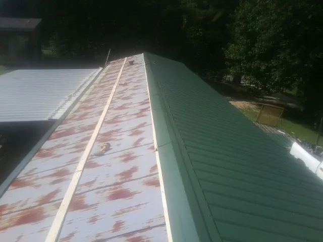 Old rusted panels beside newly installed green metal roofing — Wind Damage Roof Repair by Roofing Brothers in Pascagoula