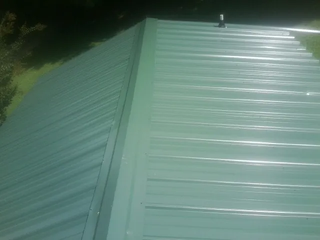 New green metal panels meeting at the ridge of a roof — Flat Roof Repair work by our crew in Pascagoula