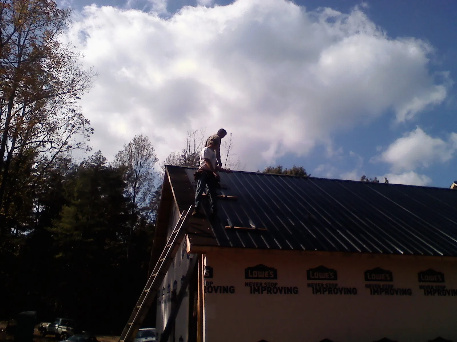 Roofer fastening dark metal panels high against a cloudy sky, from a Roof Inspection job in Pascagoula