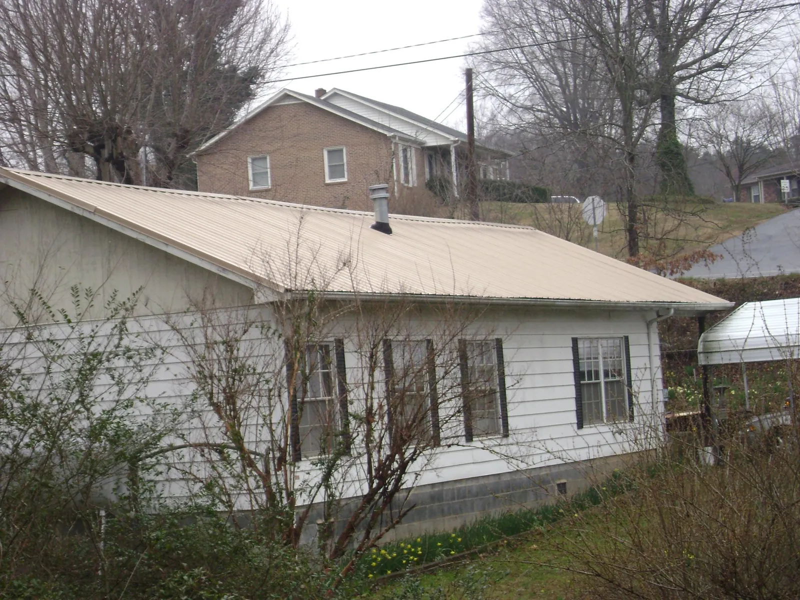 Tan metal roof on a white sided house set into a hillside — Commercial Roofing by Roofing Brothers in Pascagoula